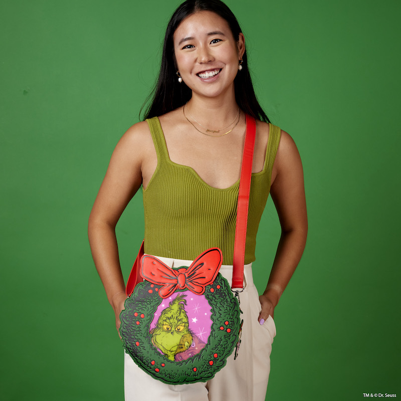 Woman wearing the How the Grinch Stole Christmas Crossbody Bag, wearing a green top and white pants, standing against a green background.
